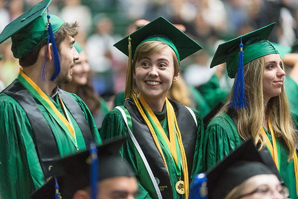 Students in graduation gowns smile for a camera