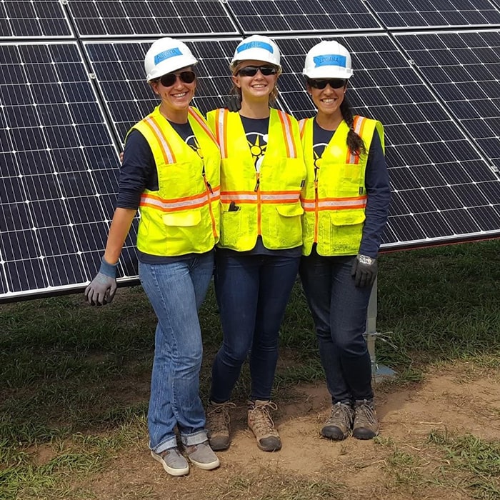 A group of three Impact MBA students pose for a photo in front of a solar panel