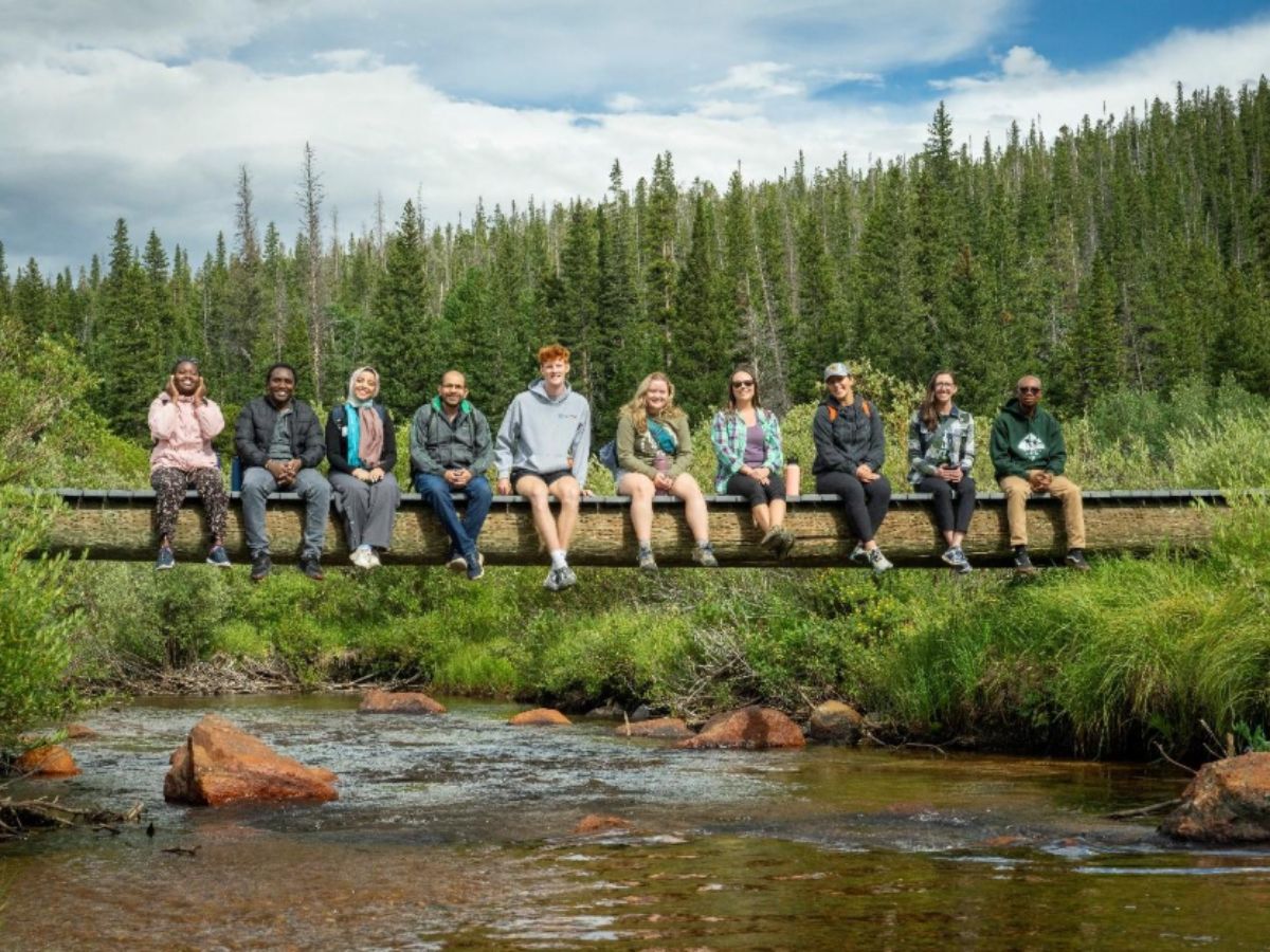 Impact MBA students and staff sit smiling for a photo along a bridge on the CSU Mountain Campus.