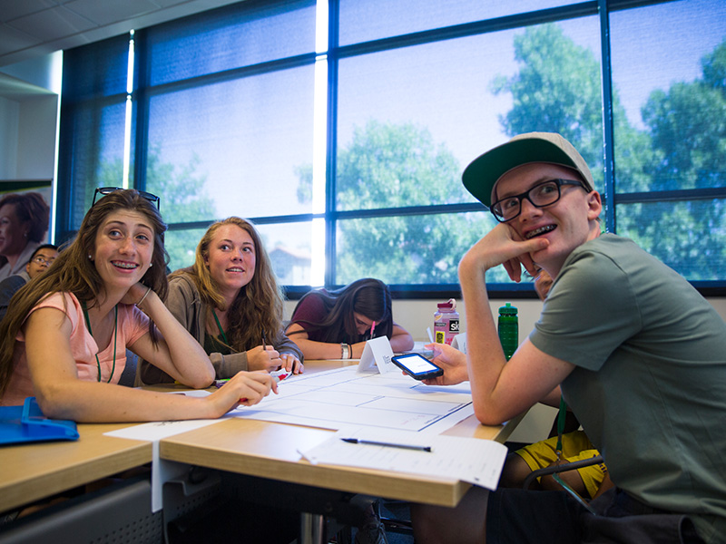 Three high school students smile as they listen to a summer business program presentation