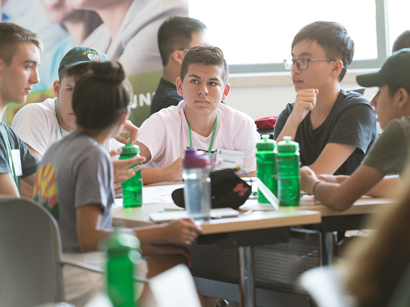 A group of high school students are seated at a table during a class discussion