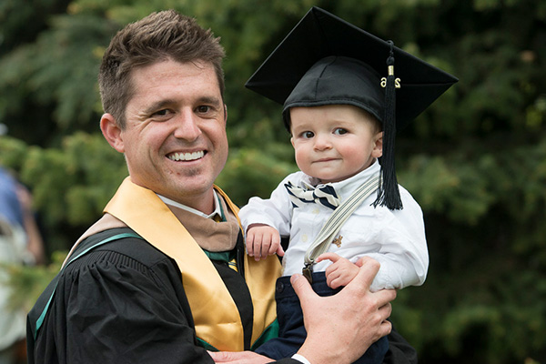 A young man holds his baby during a graduation ceremony