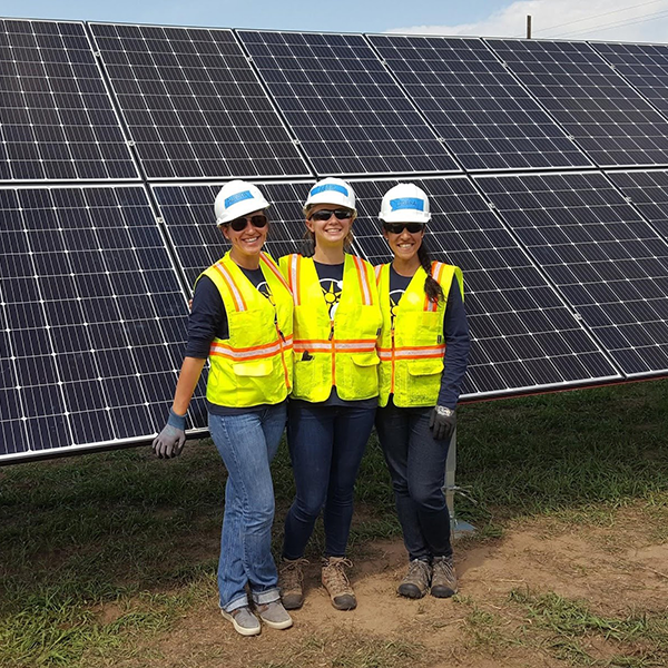 Impact MBA students pose for a photo in front of a solar panel during a day of fieldwork.