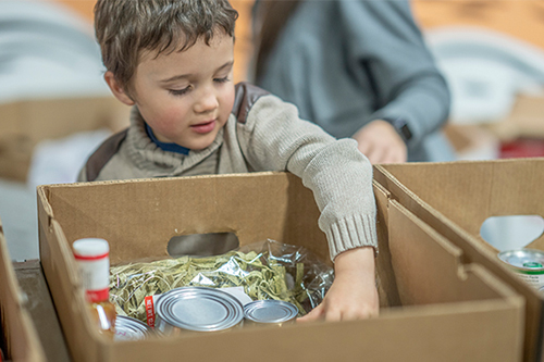 A young boy reaches into a box of food