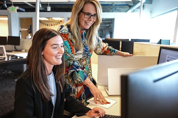 MBA students and a professor discuss an assignment in the Mosaic MBA classroom as virtually-participating students look on in the background.