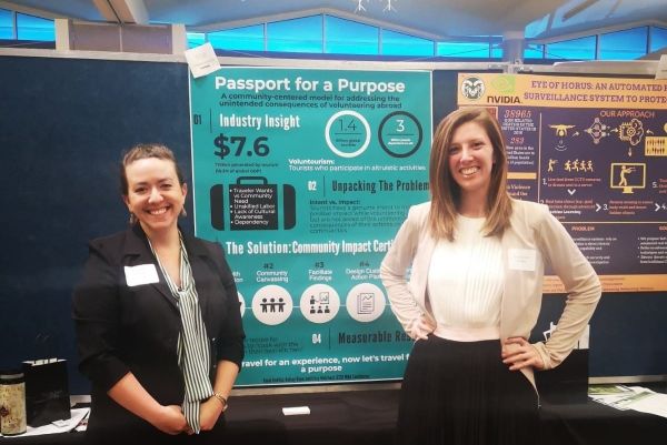 Two women pose for a photo in front of a research presentation poster.