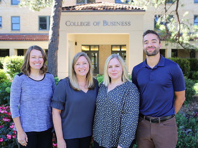 The four members of the College of Business Graduate Program Enrollment Counseling team stand in front of Rockwell Hall