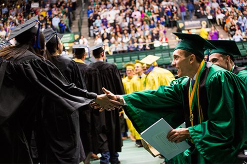 Students at graduation shake hands in congratulations